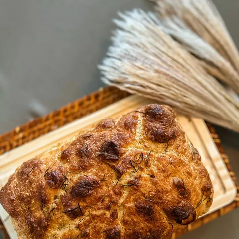 Focaccia italiana dourada, alta e coberta de alecrim, sobre tábua de madeira