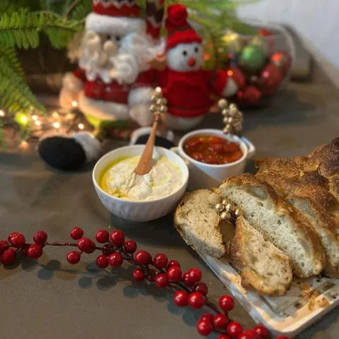 Focaccia fatiada com coalhada seca e tomate confit sobre mesa decorada para o Natal, com enfeites vermelhos e luzes